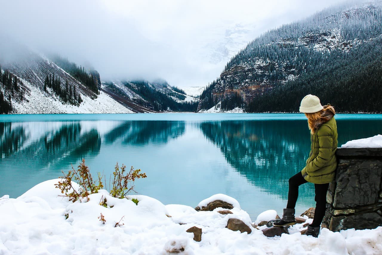 Foto original de lago de montaña nevada con agua turquesa y una persona sentada a la derecha